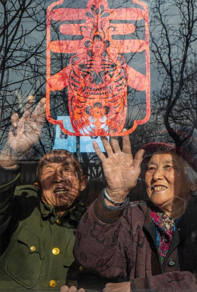 臘月里，霍州市師莊鄉(xiāng)馮南垣村村民師榮光(左)在災(zāi)后重建的新家里貼窗花。(霍州市委宣傳部供圖)