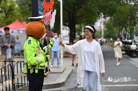 6月7日上午9時(shí)，隨著鈴聲的響起，2023年江西高考正式開考，江西省的53.57萬考生以縣（區(qū)）為單位隨機(jī)安排在全省256個(gè)考點(diǎn)、18968個(gè)考場參加高考。圖為“小熊交警”和考生擊掌鼓勵(lì)。 人民網(wǎng)記者 時(shí)雨攝