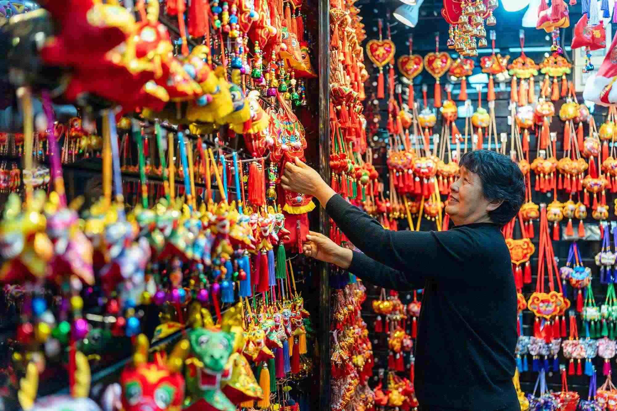 2023年12月11日，金華義烏國際商貿(mào)城，龍年喜慶用品掛滿攤位，顧客正在挑選中。