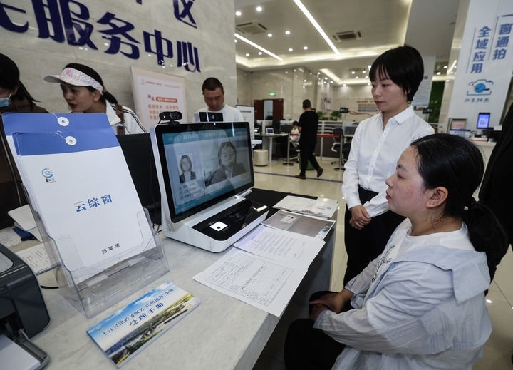 在浙江省嘉興市秀洲區(qū)王江涇鎮(zhèn)便民服務(wù)中心的“跨域通辦·云綜窗”窗口，辦理開業(yè)登記的個體工商戶（右一）通過該系統(tǒng)與江蘇省蘇州市吳江區(qū)盛澤鎮(zhèn)行政審批局工作人員視頻連線，進行身份讀取及材料線上審核（2024年5月9日攝）。新華社記者 徐昱 攝