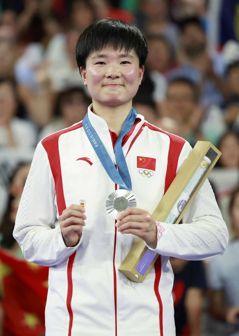 巴黎奧運(yùn)會(huì)羽毛球女子單打亞軍、中國(guó)選手何冰嬌在頒獎(jiǎng)儀式上一手握著銀牌，一手握著西班牙奧委會(huì)徽章（2024年8月5日攝）。新華社記者 任正來(lái) 攝