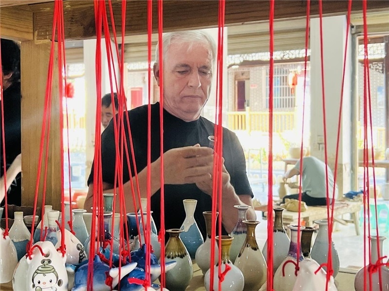 鄉(xiāng)愁如同一根根紅線，將游子與故鄉(xiāng)永遠(yuǎn)地牽連到一起?；逄账囄幕瘎?chuàng)意一條街的母氏陶藝館內(nèi)，紅線吊著陶瓶，思緒游走萬里。摩爾多瓦“信息標(biāo)簽”通訊社社長亞歷山大·塔納斯端詳著館內(nèi)展示的陶藝作品，并挑選出心儀的小擺件帶回摩爾多瓦，也帶走花茂村的“鄉(xiāng)愁”。（張亞欣攝）
