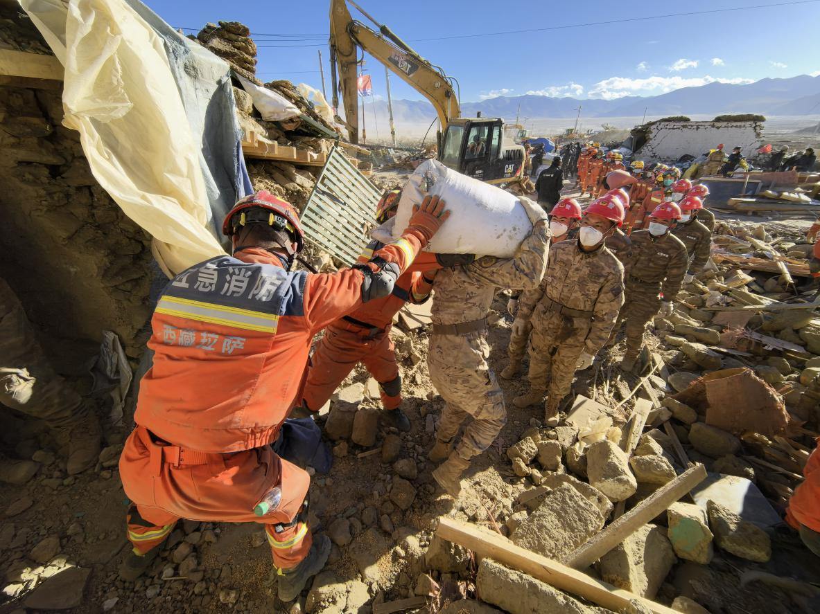 1月11日，定日縣長所鄉(xiāng)古榮村，應急消防等救援人員排隊接力搶運掩埋在倒塌房屋下的群眾財物。人民日報記者楊翹楚攝
