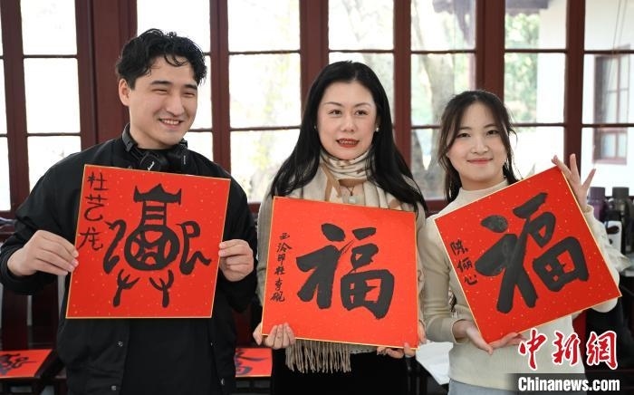1月20日，外籍留學(xué)生和西泠印社社員李硯(中)展示各自創(chuàng)作的福貼。當日，來自巴西、馬來西亞、加納、哈薩克斯坦的外籍留學(xué)生在浙江杭州西泠印社體驗福貼、春聯(lián)和篆刻，感受古老的中國傳統(tǒng)文化。中新社記者 王剛 攝