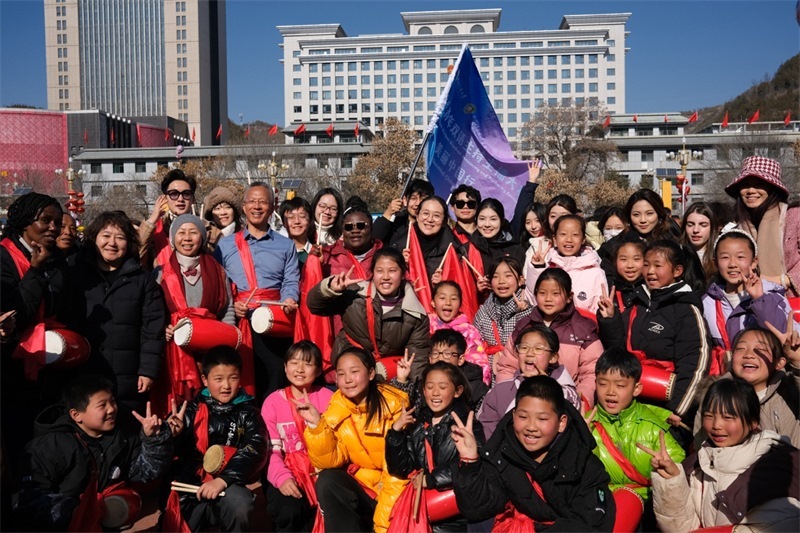 中外青年學(xué)子在安塞文化廣場觀看陜北腰鼓和大秧歌表演后合影留念，大家踏著鼓點(diǎn)共舞，翻飛的紅綢與躍動的身影交織，在黃土地廣場上繪出一幅生動的陜北民俗互動畫卷